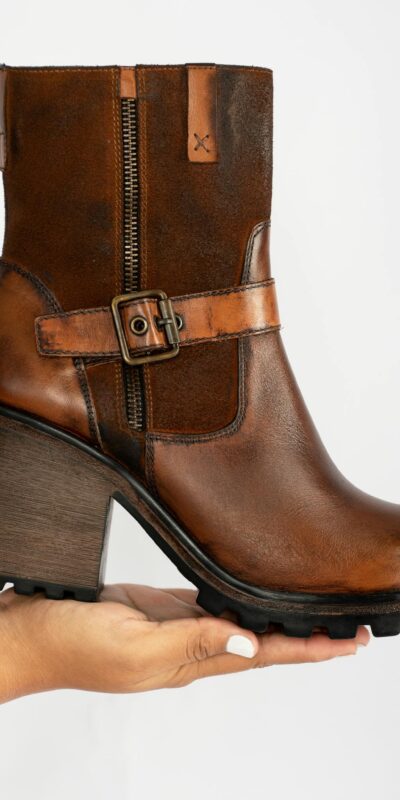 Elegant brown leather ankle boot with block heel and buckle detail, showcased on a hand.
