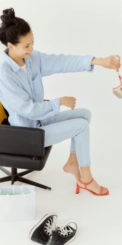 Smiling woman in casual outfit trying on bright sandals in a stylish setup.