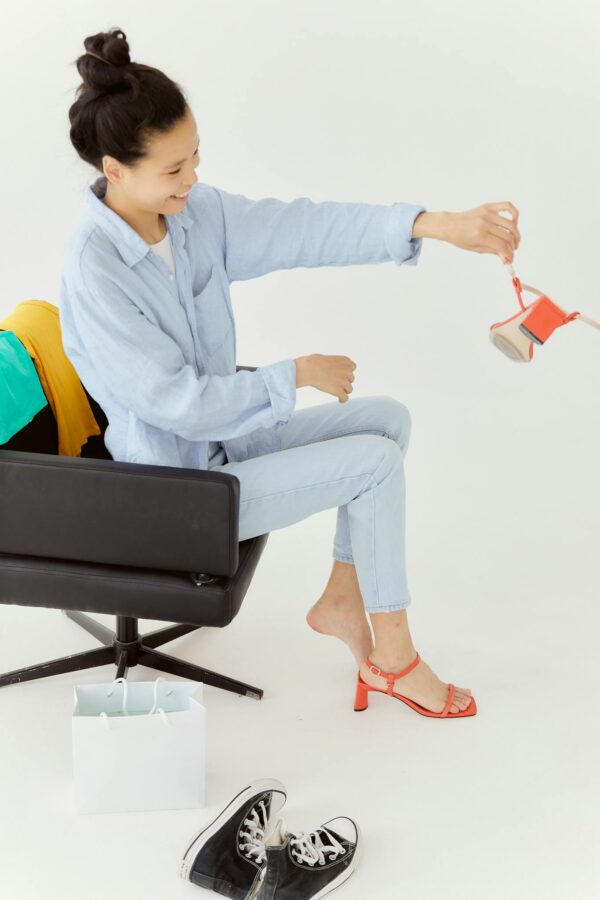 Smiling woman in casual outfit trying on bright sandals in a stylish setup.